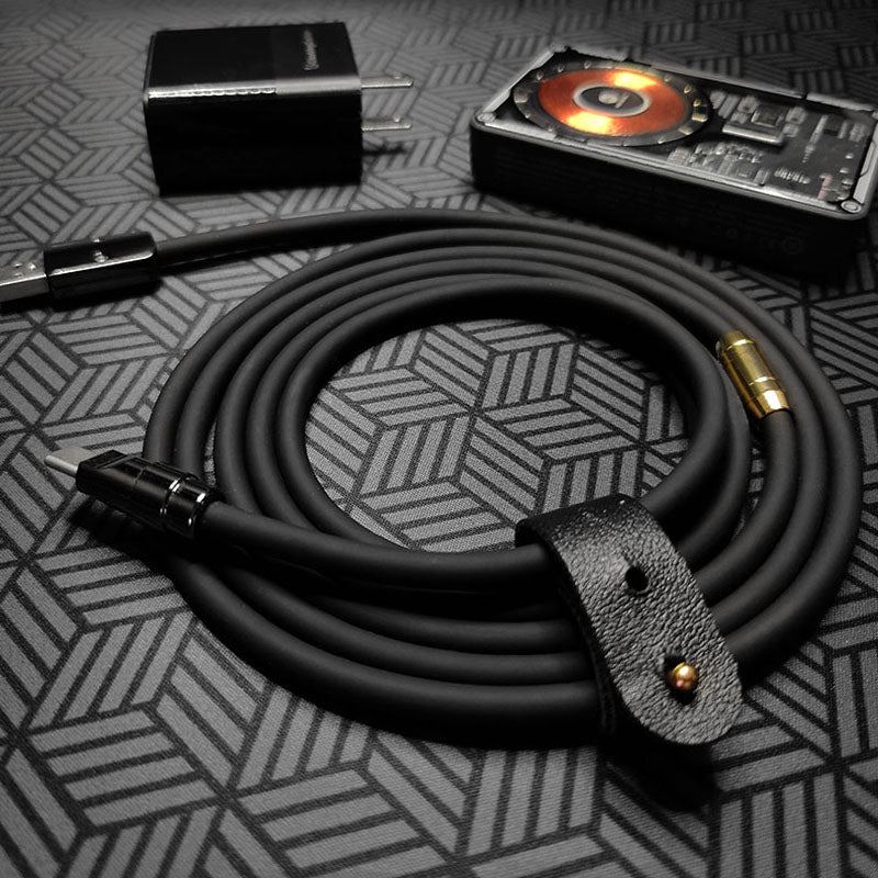 Black charging cable coiled with leather strap, next to wall plug and power bank